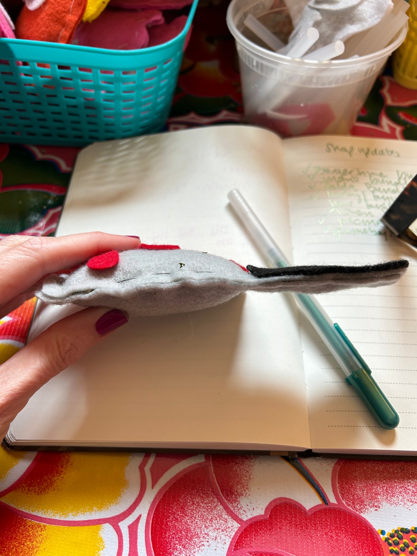 A person holding a catnip cat toy for sale. The item is made out of felt to resemble a cleaver. The view is of the side of the cat toy. There is a notebook and pen in the background.