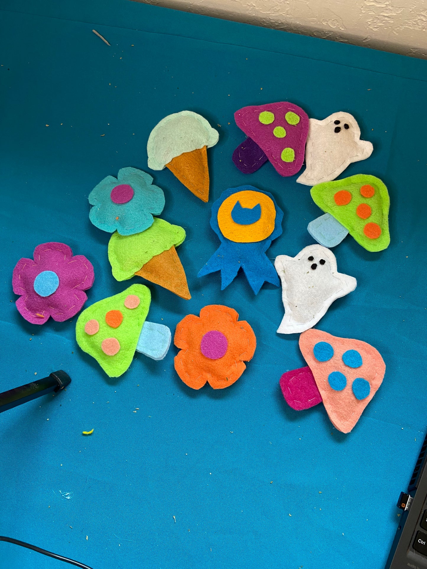 A collection of cat toys for sale. Toys are made of felt, there are ghosts, mushrooms in various colors, ice cream cones, flowers and an award ribbon.