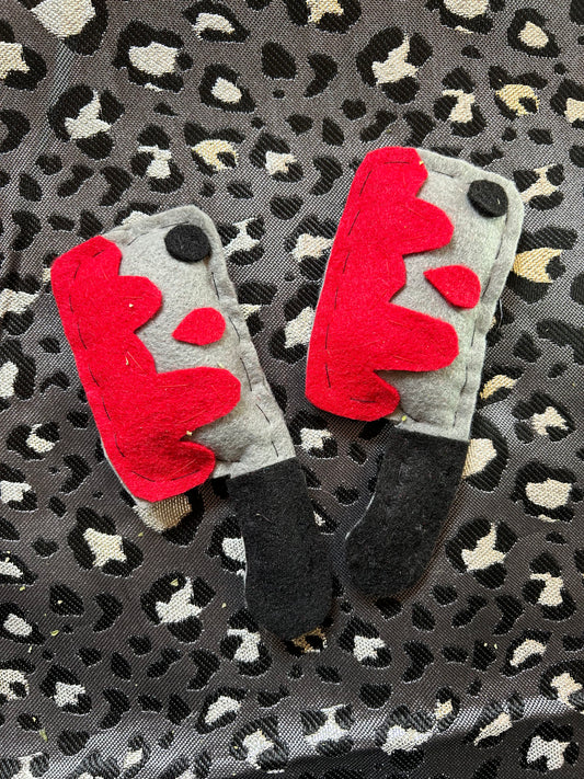 A set of two catnip cat toys for sale. Toys are made out of felt to resemble cleavers with blood on them. They are on a grey animal print backgrounf